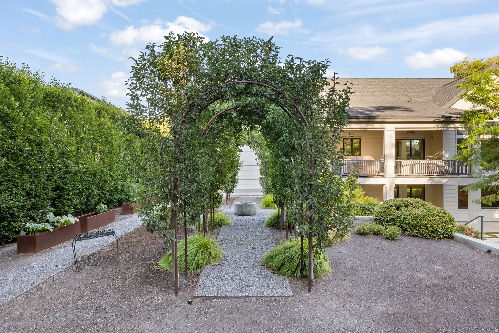 Gravel pathway featuring an arbor with mature foliage, leading to a multi-level exterior with balconies
