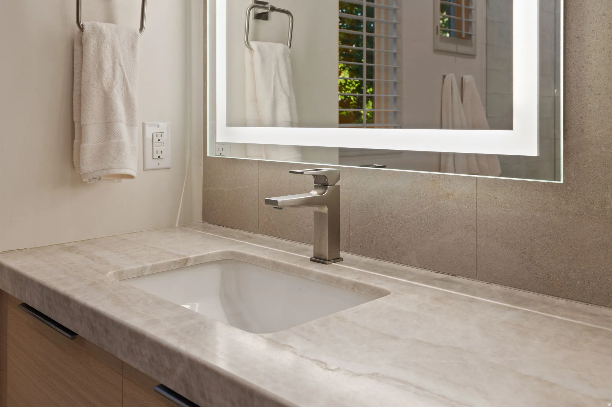 Integrated rectangular sink with a single-handle faucet, illuminated mirror, stone countertop, and tile backsplash