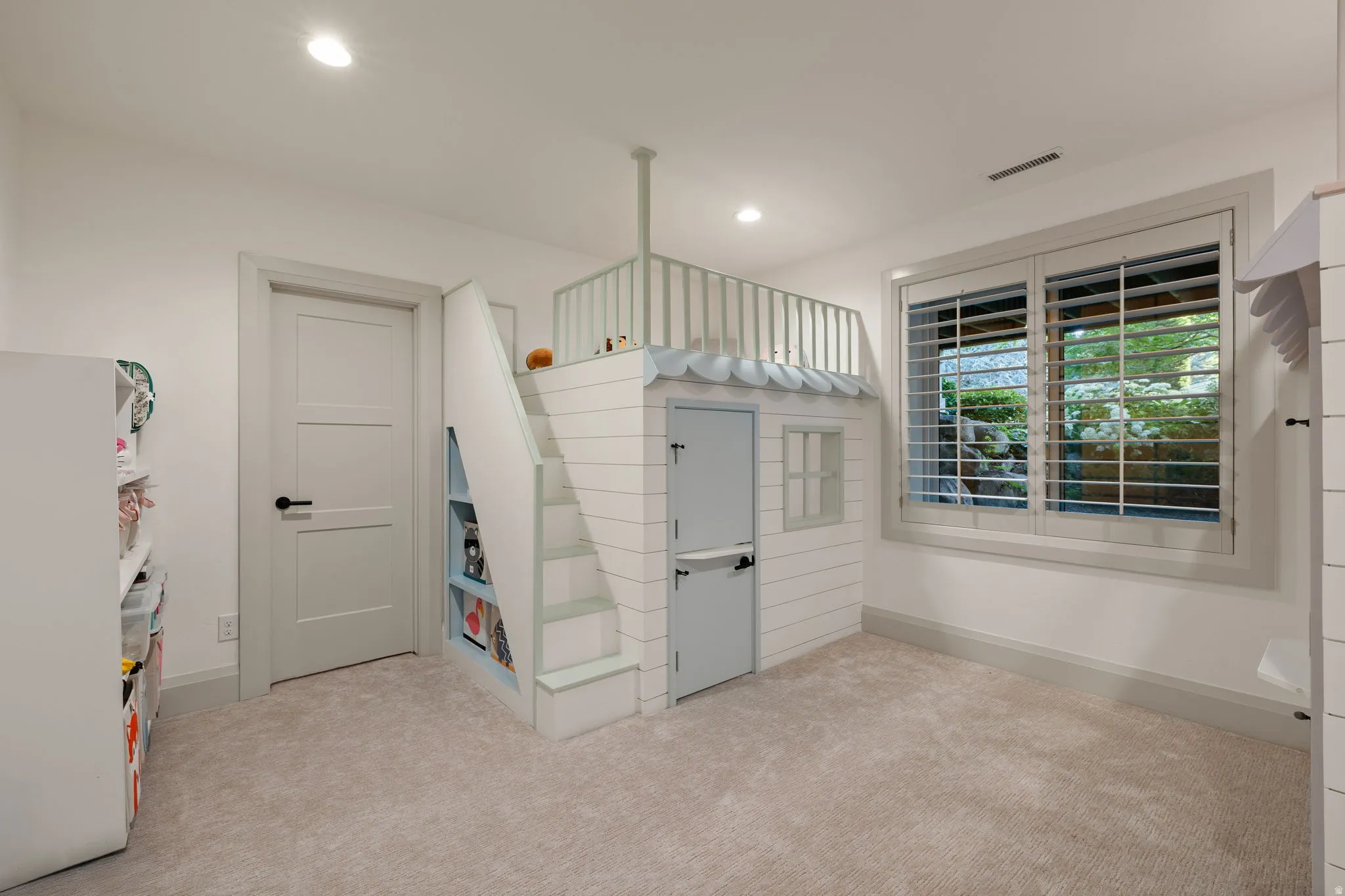 Custom built-in playhouse with integrated staircase and upper platform, white shiplap-style siding, and a light gray door