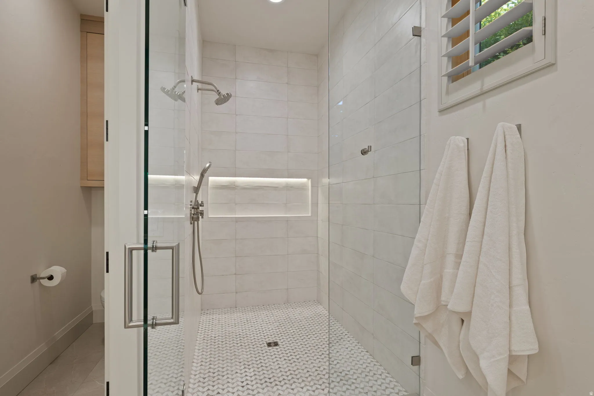 Walk-in shower featuring a glass enclosure, white subway tile walls, and a herringbone-patterned tile floor