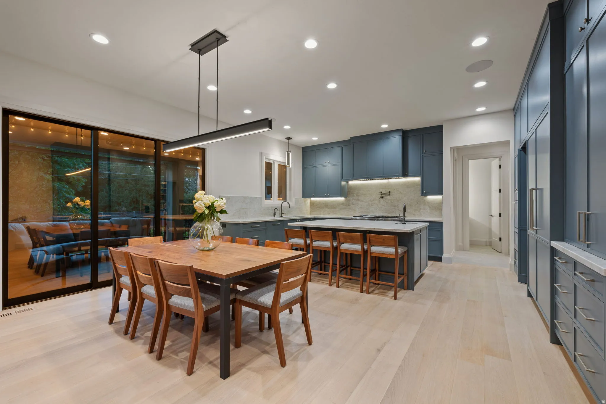 Open-concept kitchen and dining area featuring light wood-finish flooring, a kitchen island with seating, dark blue cabinetry, and a full-height tile backsplash