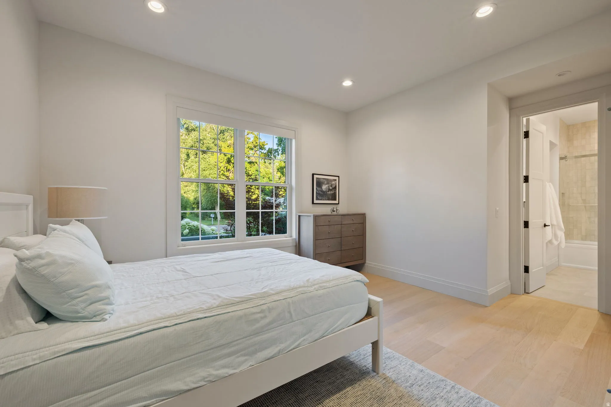Spacious room featuring hardwood flooring, recessed lighting, and a large window overlooking lush greenery