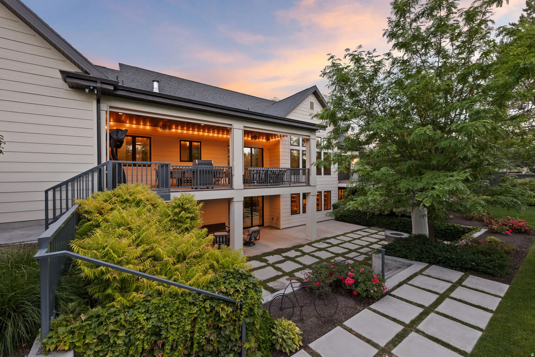 Multi-level outdoor living spaces featuring a covered upper deck with railing, a covered lower patio, and a concrete paver walkway