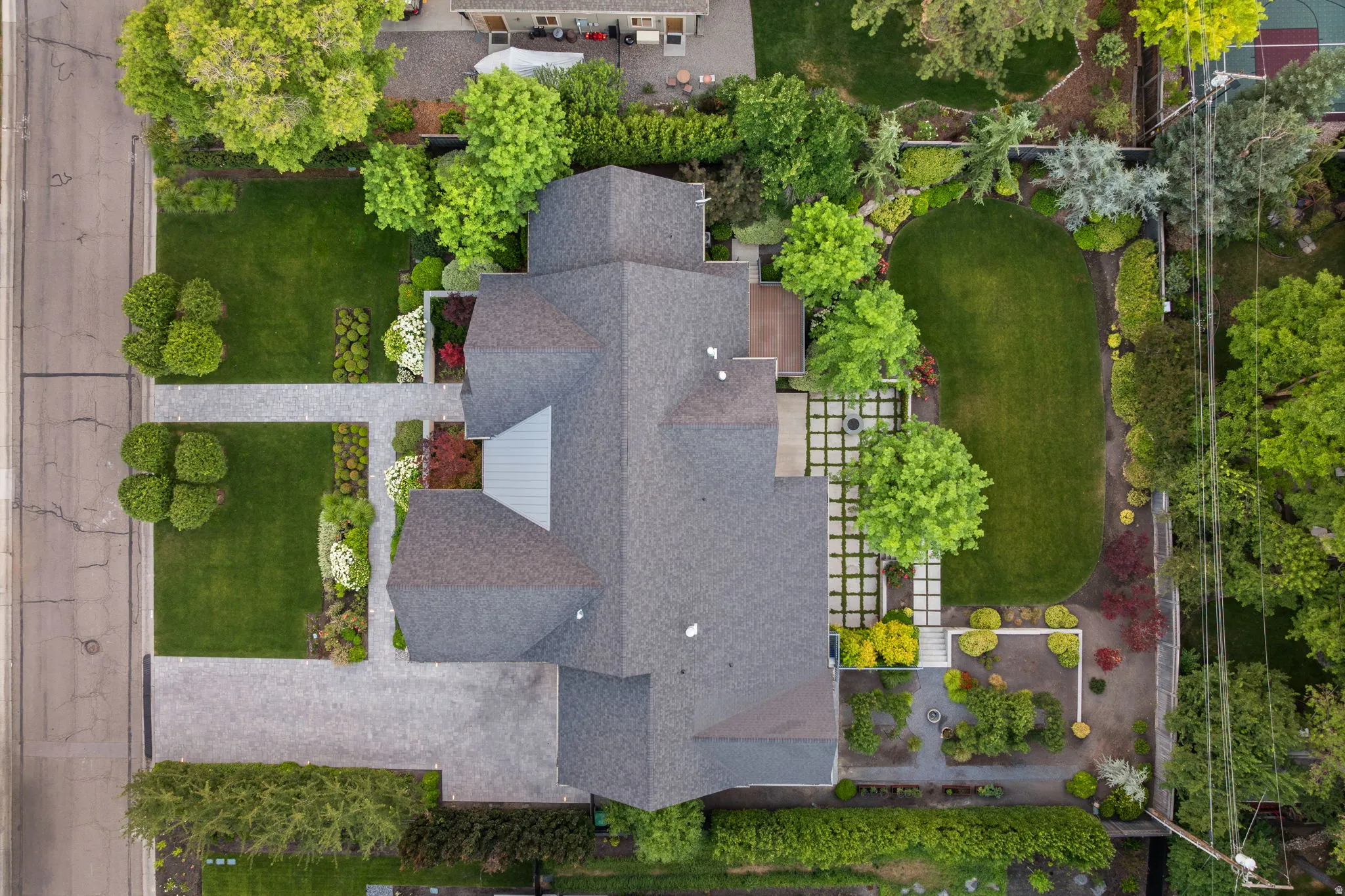 Contemporary residence featuring a multi-gabled roofline, extensive manicured lawns, mature trees, and a geometric hardscaping design