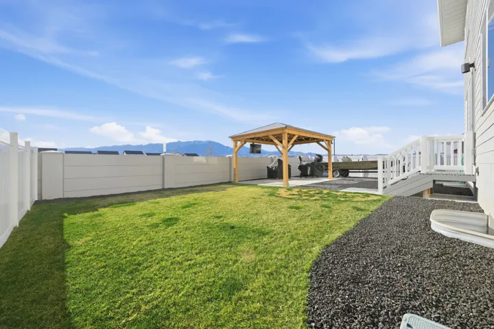 Spacious backyard featuring a manicured lawn, a wooden gazebo, and a gravel area