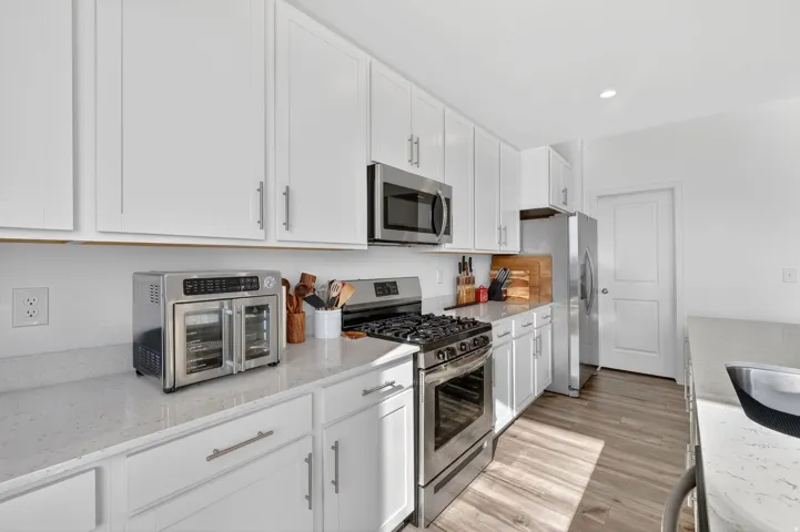 Modern kitchen featuring white shaker cabinetry, stainless steel appliances, light-toned countertops, wood-finish flooring, and recessed lighting