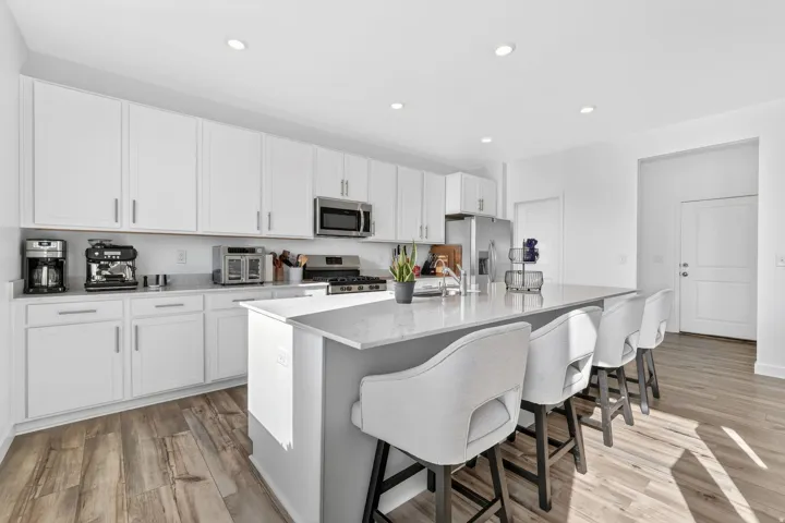 Kitchen featuring white cabinetry, stainless steel appliances, a large island with a light-toned countertop, recessed lighting, and wood-finish flooring
