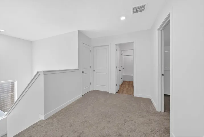 Carpeted upper-level landing featuring white doors, recessed lighting, and a partial staircase with a white railing