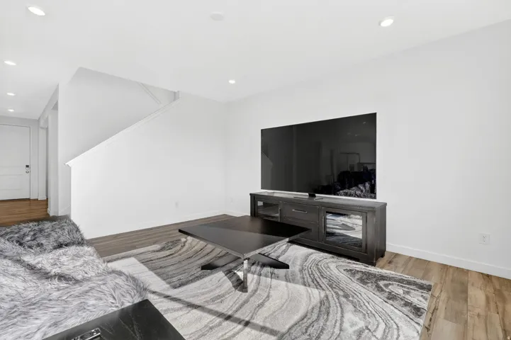 Bright living space featuring recessed lighting, wood-finish flooring, a contemporary entertainment console, and a staircase with a white railing
