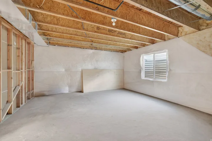 Unfinished basement space with concrete flooring, exposed wood joists, and a framed wall