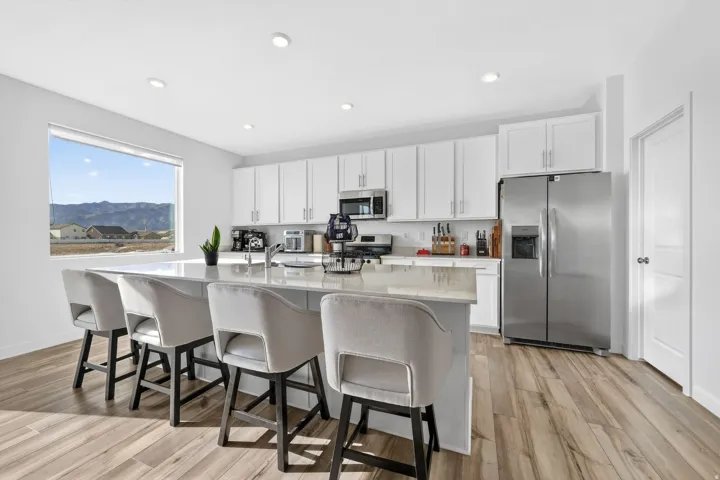 Expansive kitchen featuring a large island with seating, stainless steel appliances, white cabinetry, wood-finish flooring, and a wide window with a mountain backdrop