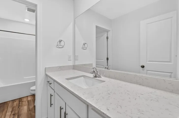 Bathroom vanity featuring a light-toned countertop with an integrated sink, polished chrome faucet, and white cabinetry with brushed nickel hardware