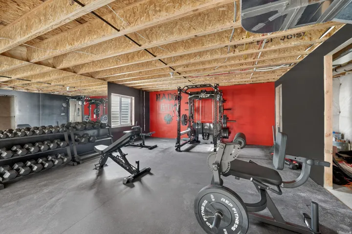 Dedicated fitness space featuring a rubberized floor, exposed wood ceiling, and a prominent mirrored wall