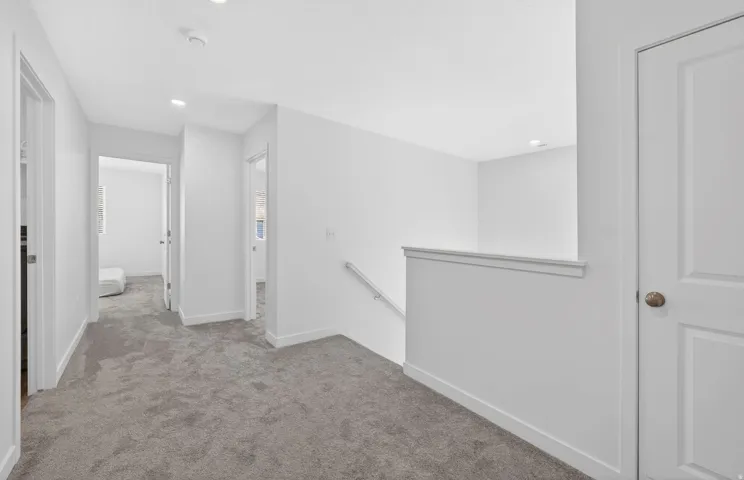 Bright upper-level hallway with recessed lighting, light gray carpet, white walls, and a white stair railing