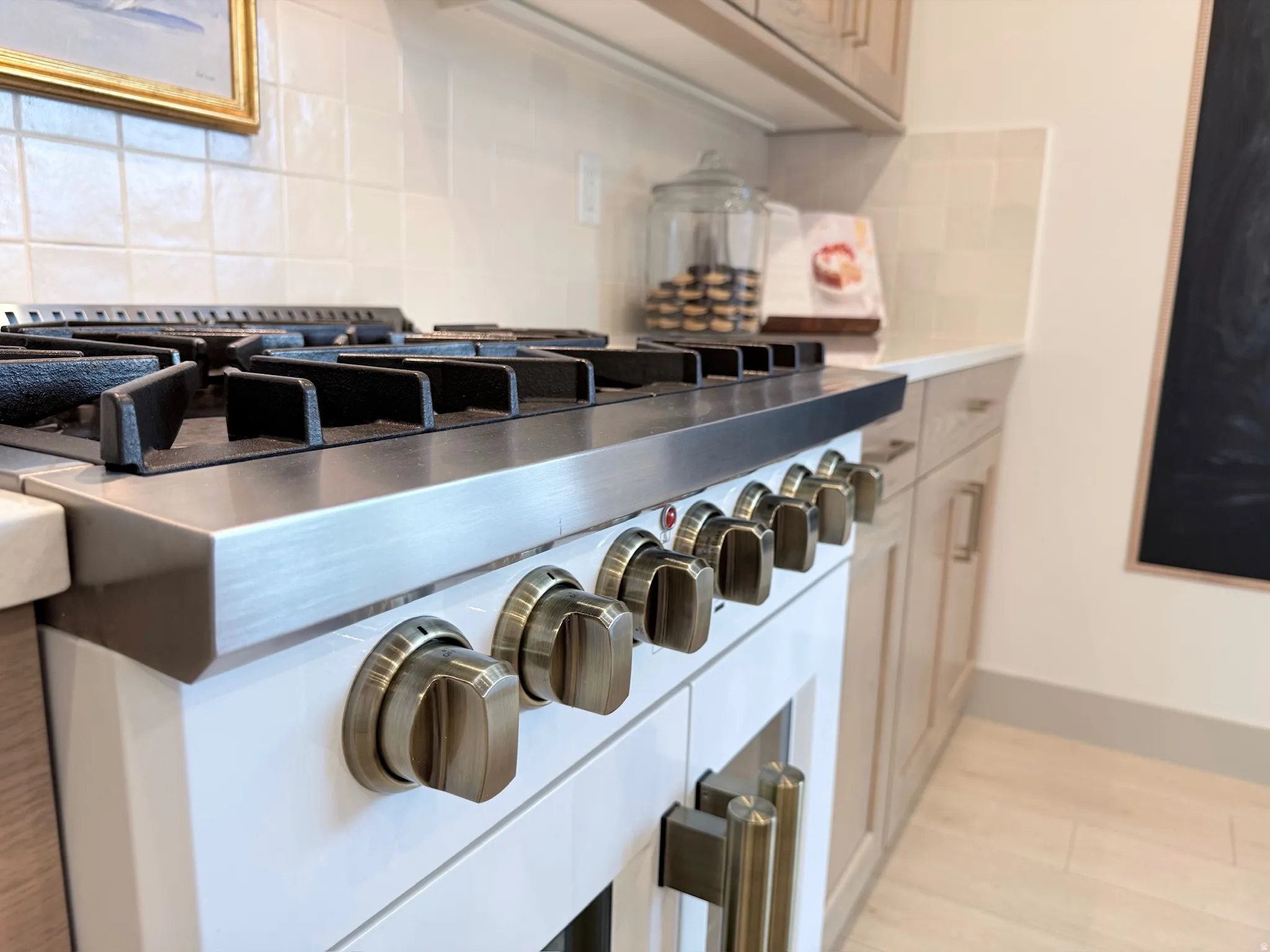 Professional-grade range with stainless steel cooktop and brass-toned hardware, set against a tiled backsplash