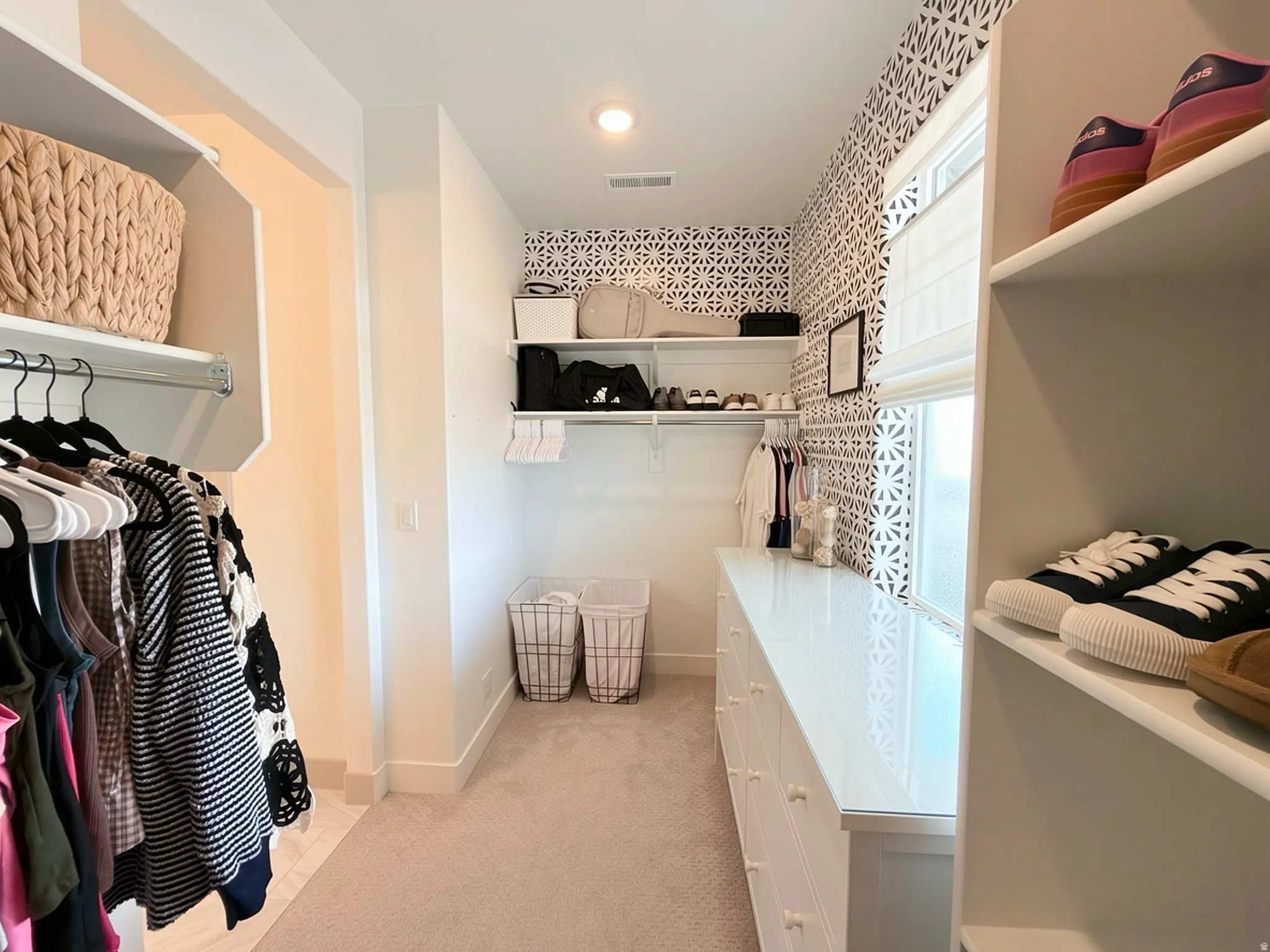 Dedicated closet space featuring white shelving, a built-in dresser with a polished surface, and patterned accent wallpaper