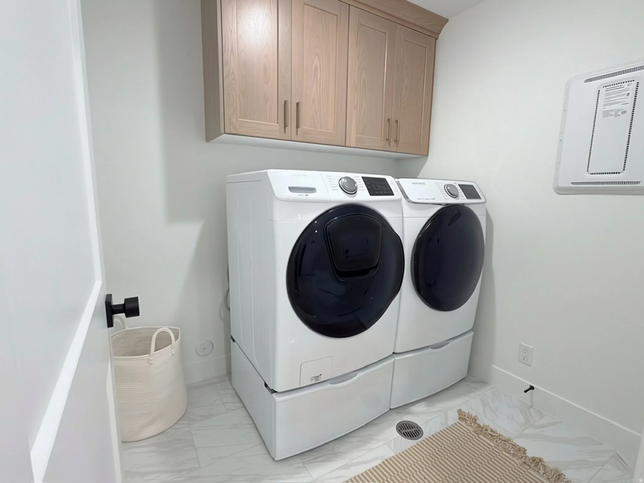 Dedicated laundry space featuring light wood-finish cabinetry, white wall paint, and marble-look floor tiling