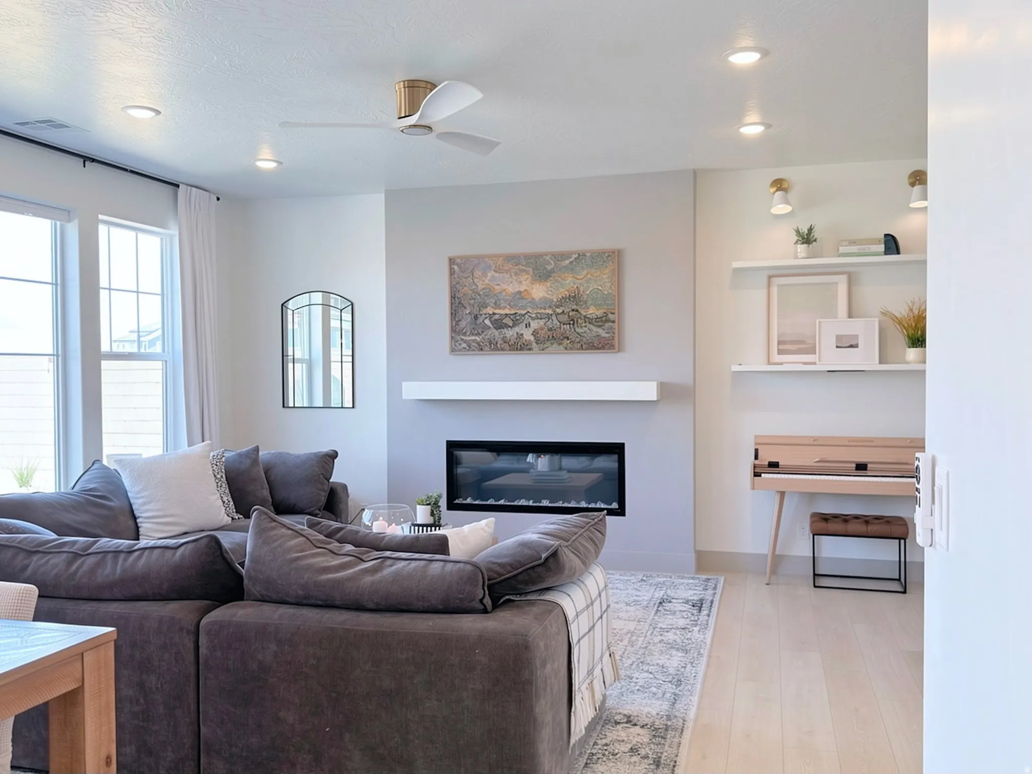 Living area featuring a modern electric fireplace with a white mantle, light wood-finish flooring, a ceiling fan with integrated lighting, recessed lighting, and large windows