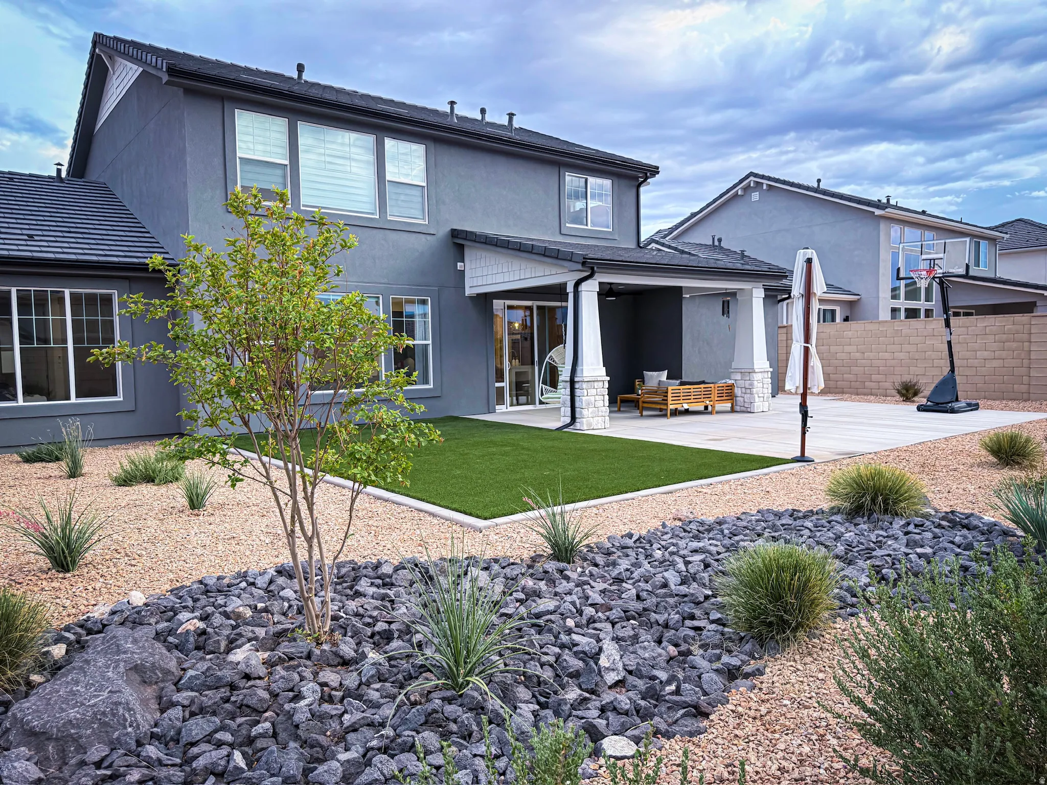 Expansive rear yard featuring a covered patio with pillars, a concrete pad, and a low-maintenance landscape design with gravel and rock beds