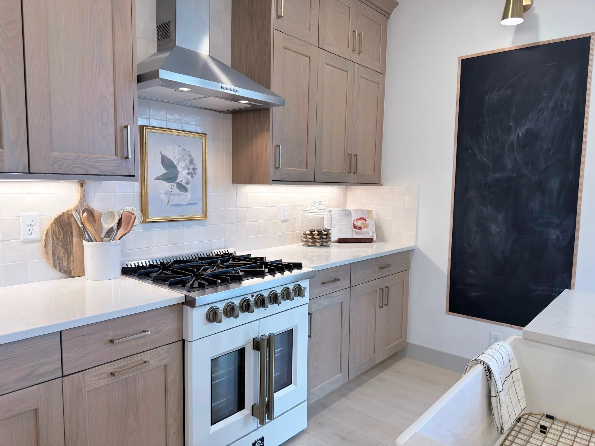 Gourmet kitchen featuring a professional-grade gas range with double ovens, stainless steel range hood, light wood-finish cabinetry, white subway tile backsplash, and light-toned countertops