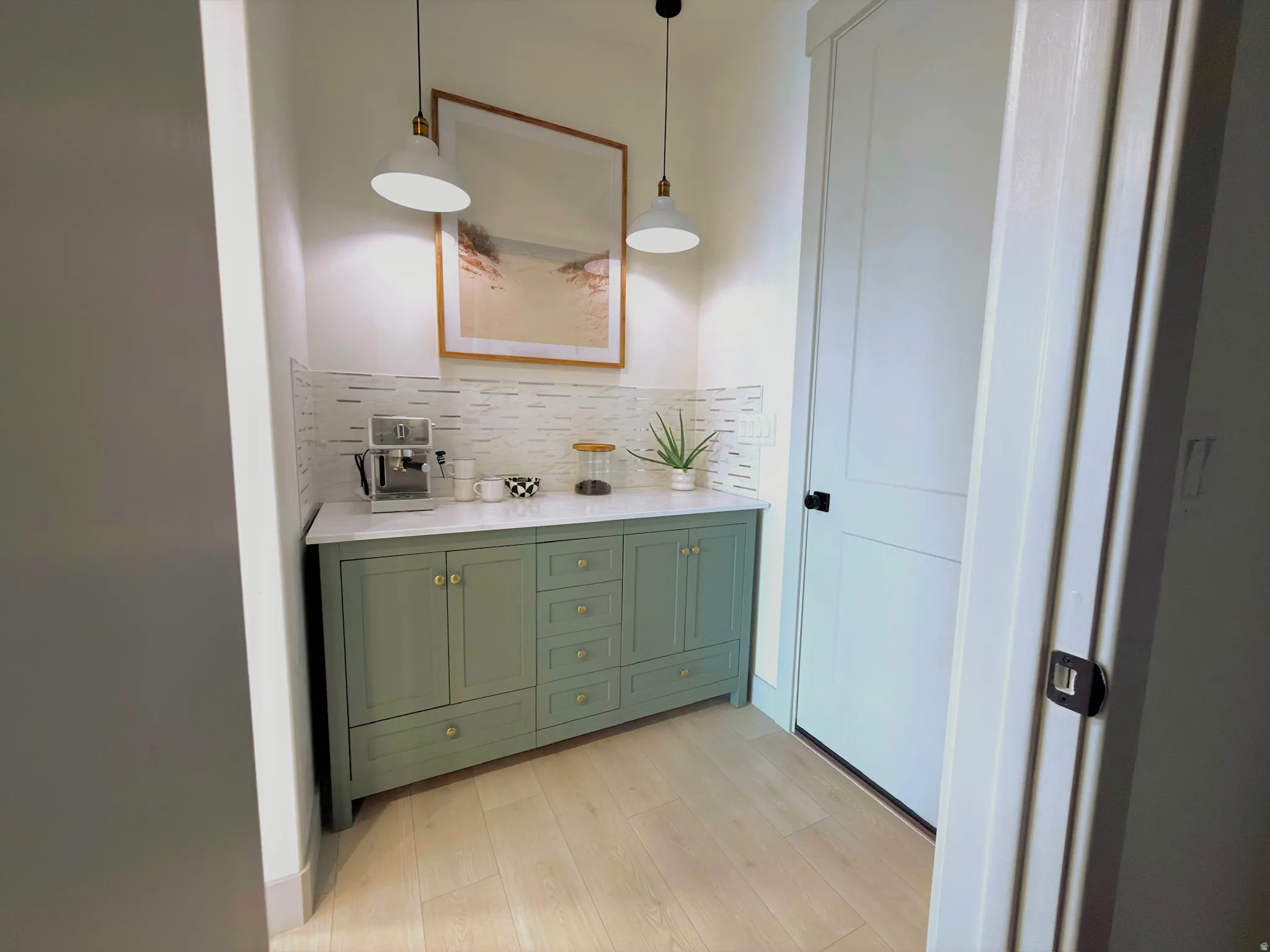 Custom built-in cabinetry with a light green finish and brass hardware, featuring a white countertop and rectangular tile backsplash
