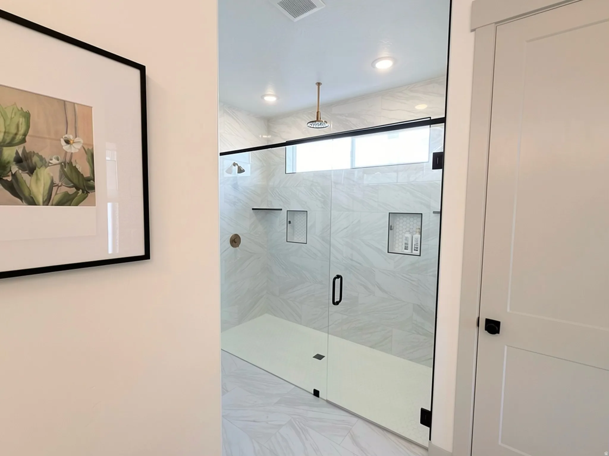 Frameless glass shower enclosure featuring white subway tile walls, a rain showerhead, a built-in shelf, and a bronze-finish shower control