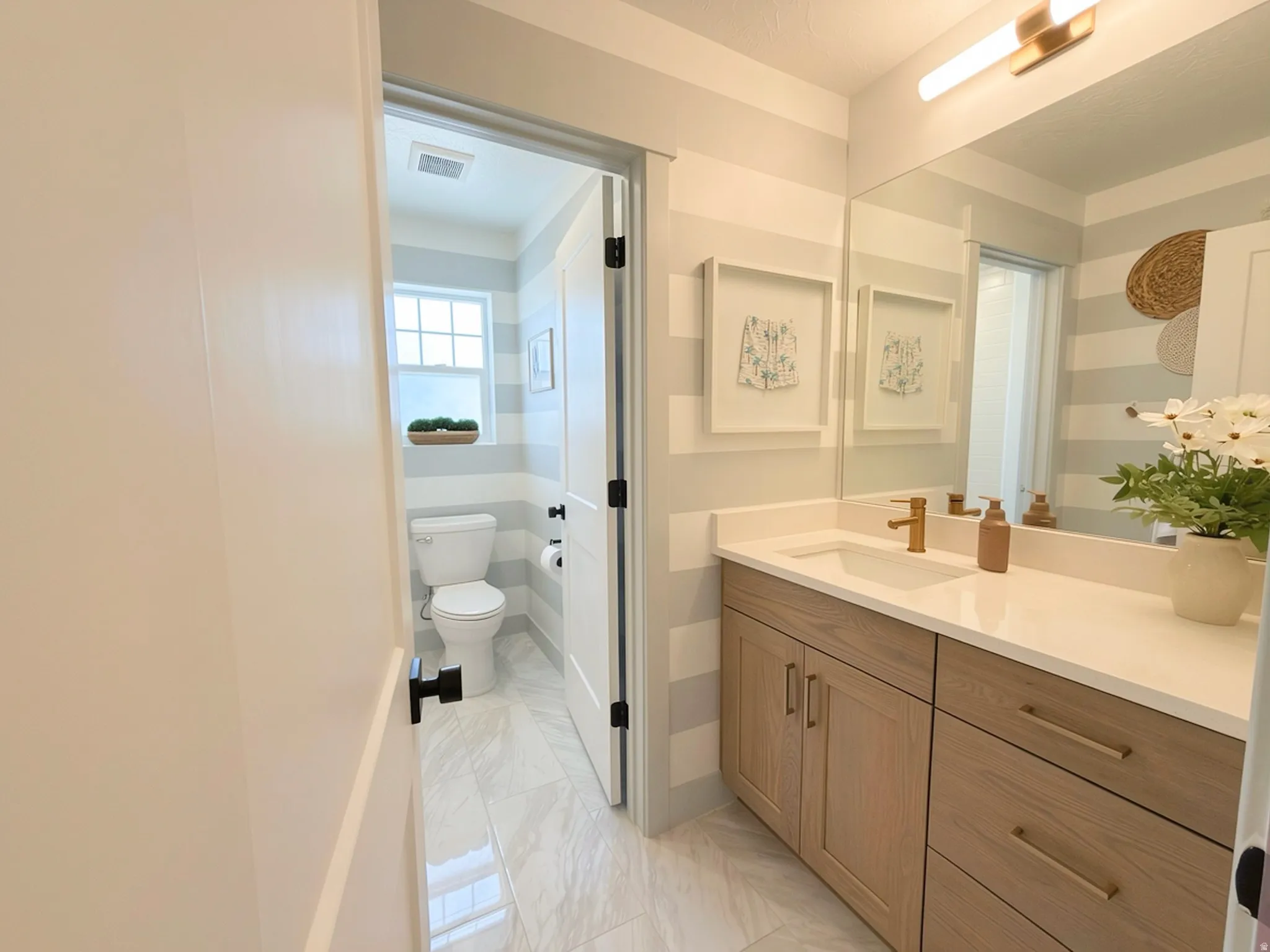 Bathroom vanity with light wood-finish cabinetry, white countertop, and gold-finish fixtures