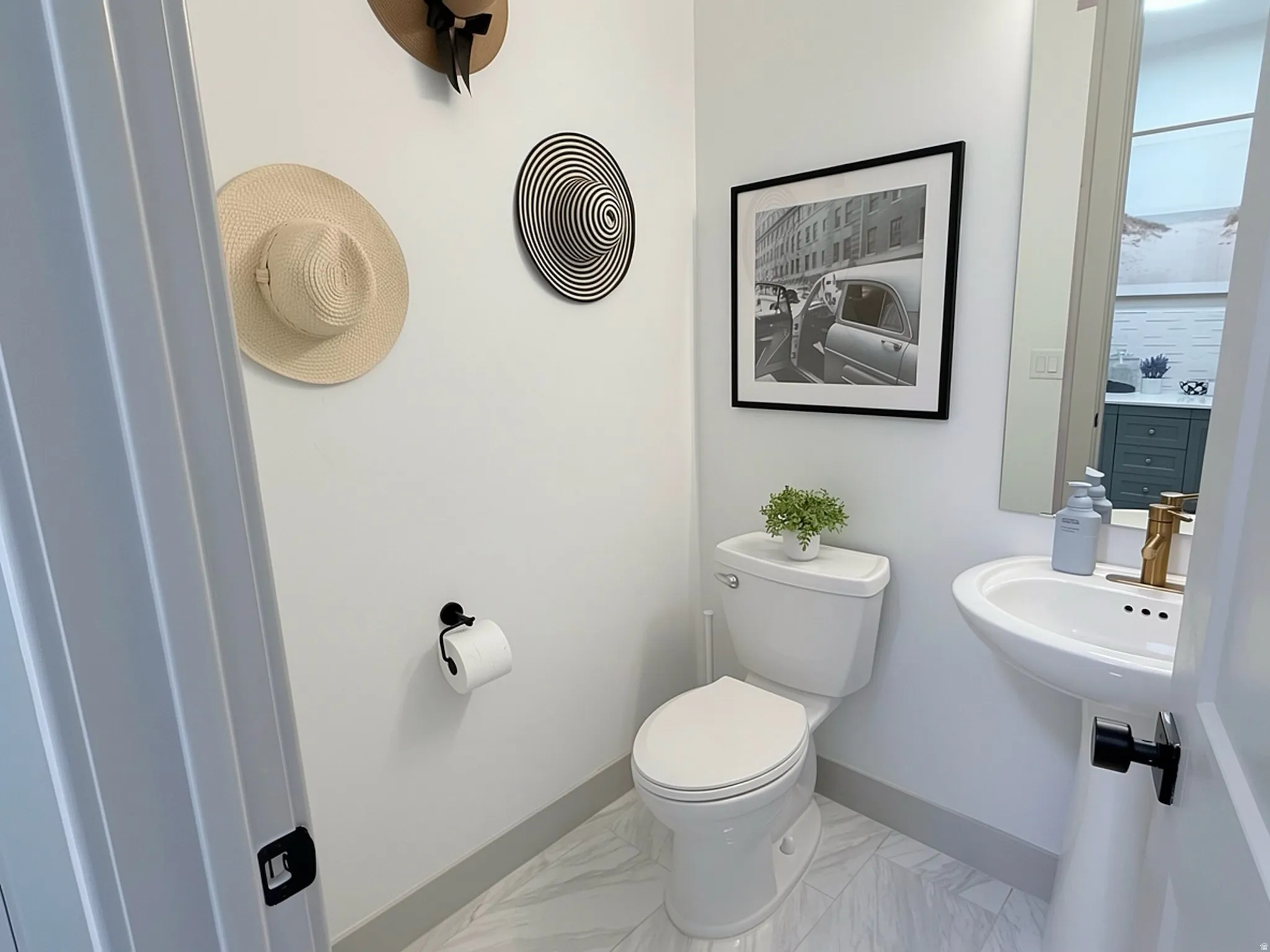 Powder room featuring a pedestal sink with a gold-finish faucet, a white toilet, and light-toned tile flooring