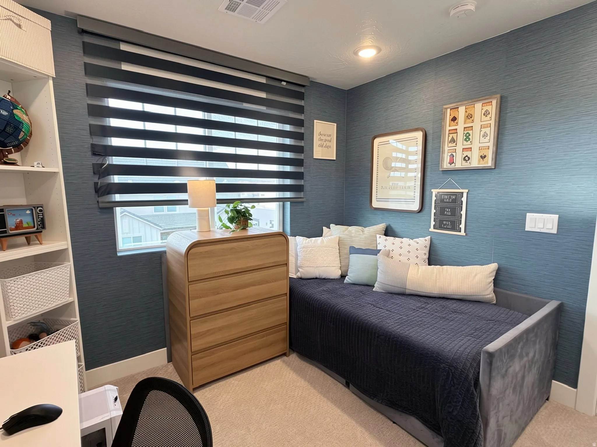 Textured wall covering, neutral carpeting, window with privacy blinds, built-in shelving, and recessed ceiling lighting