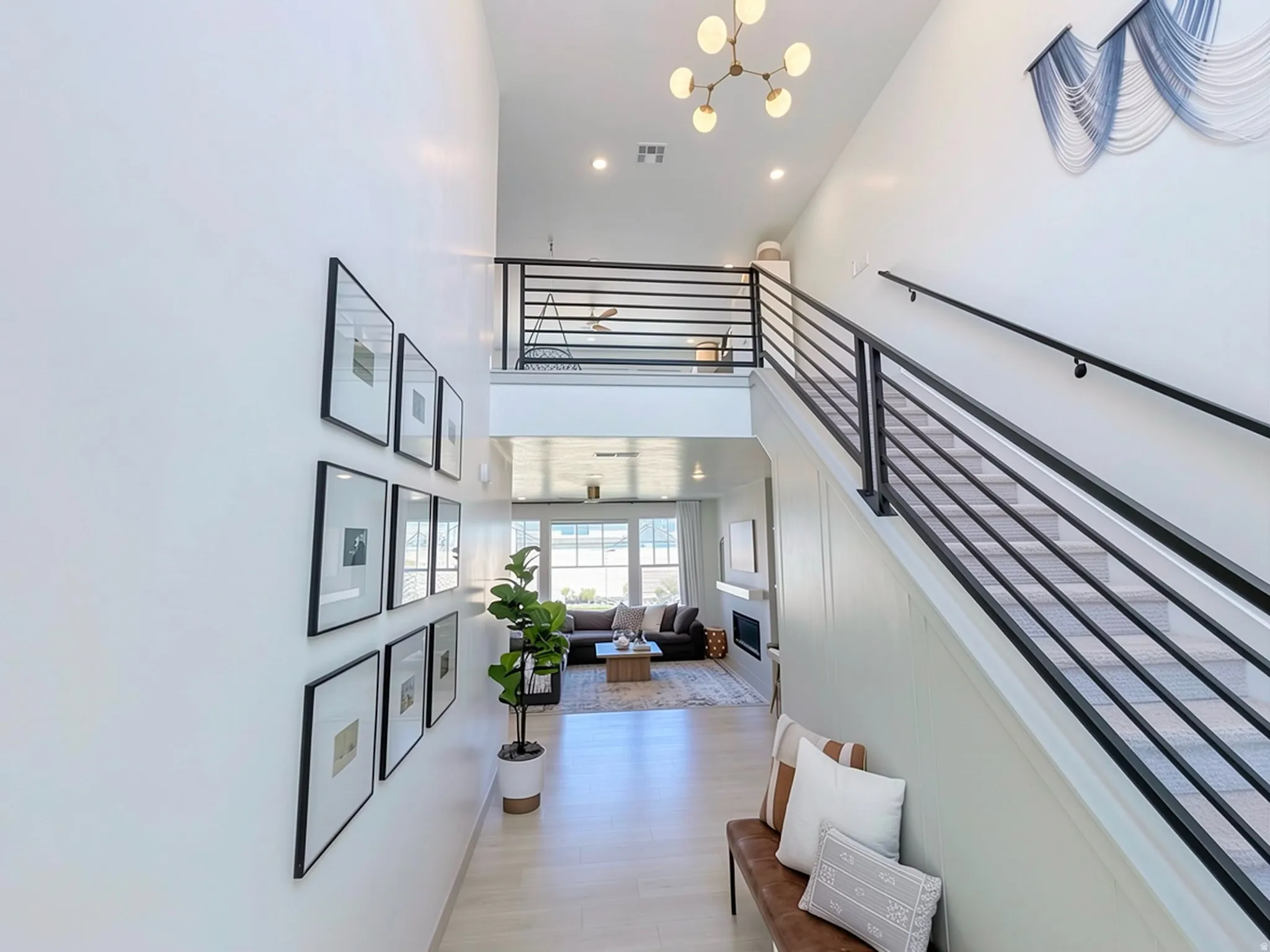 Two-story entryway with light wood-finish flooring, a contemporary chandelier, and a modern horizontal bar railing staircase