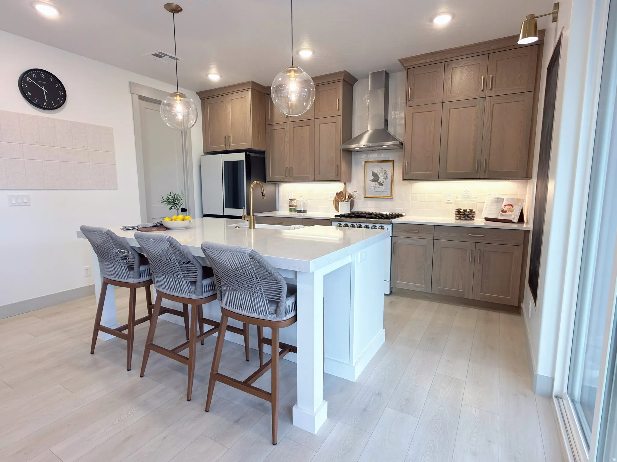 Modern kitchen featuring an expansive central island with seating for four, wood-finish flooring, light-toned cabinetry, stainless steel appliances, and pendant lighting fixtures