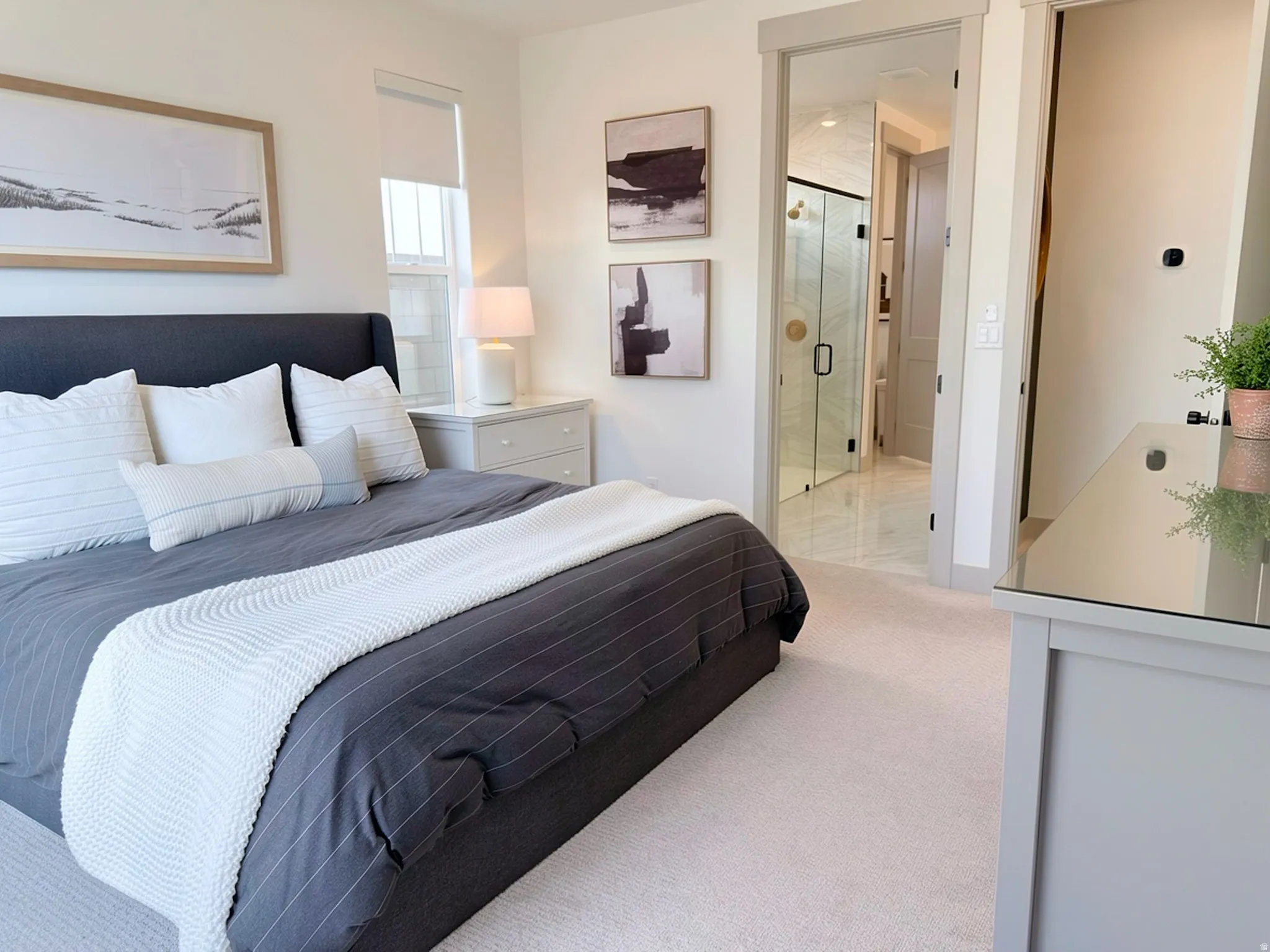 Carpeted bedroom with a window featuring a roller shade and a bedside table with a lamp