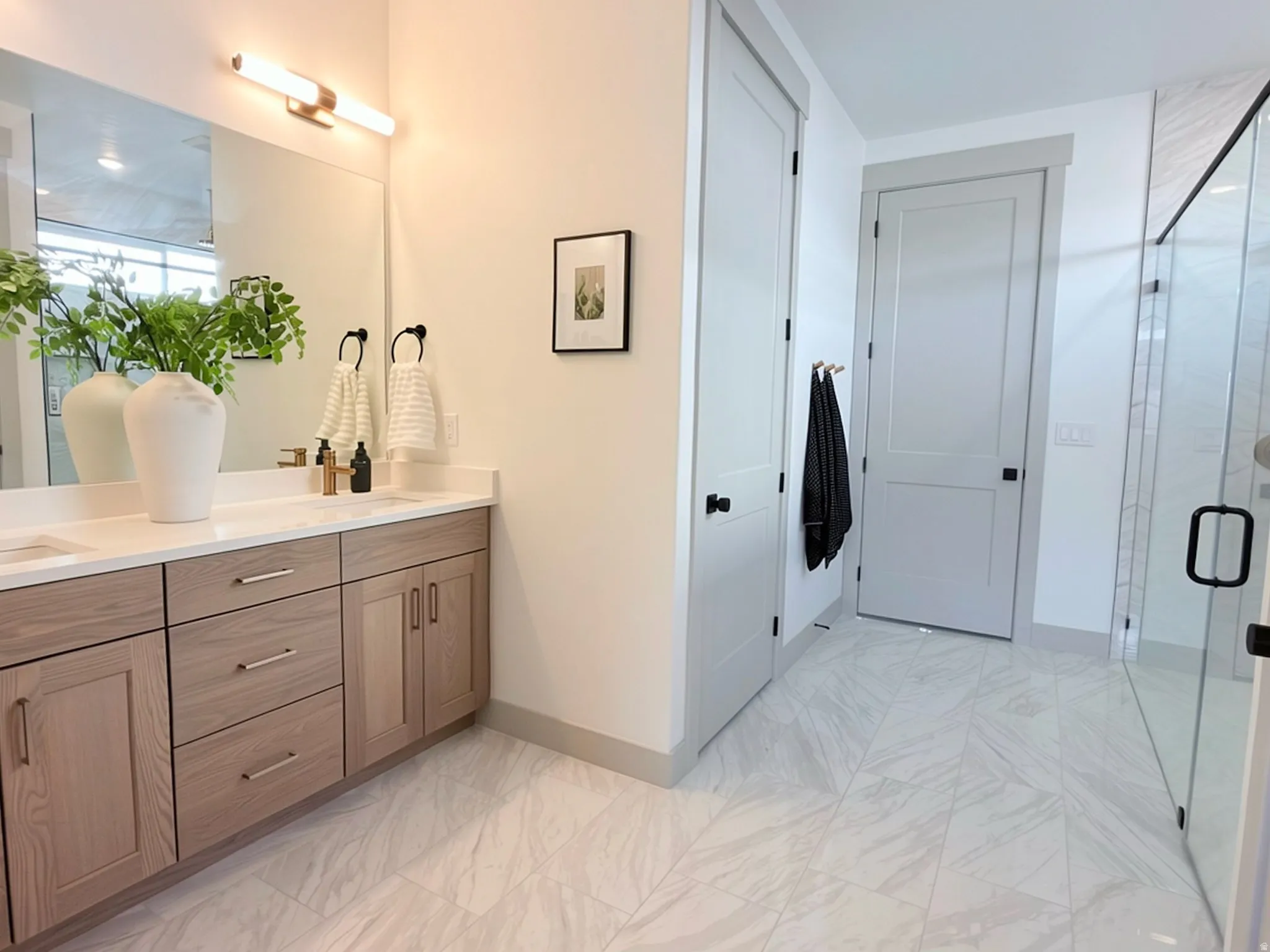 Double vanity featuring wood-finish cabinetry, light countertops, and a large mirror with integrated lighting
