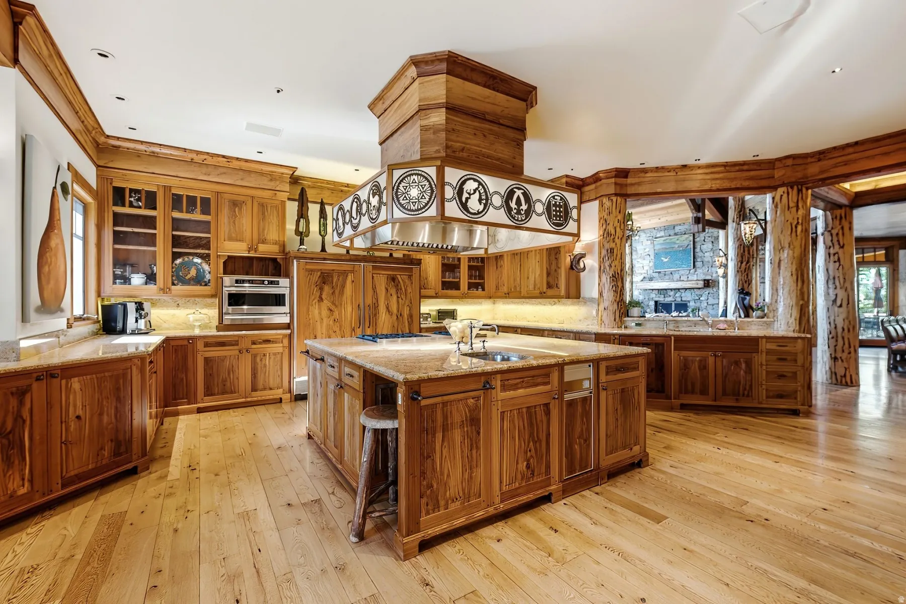 Gourmet kitchen with wood-finish flooring, extensive natural wood cabinetry, light-toned stone countertops, a large center island with integrated sink, and stainless steel appliances