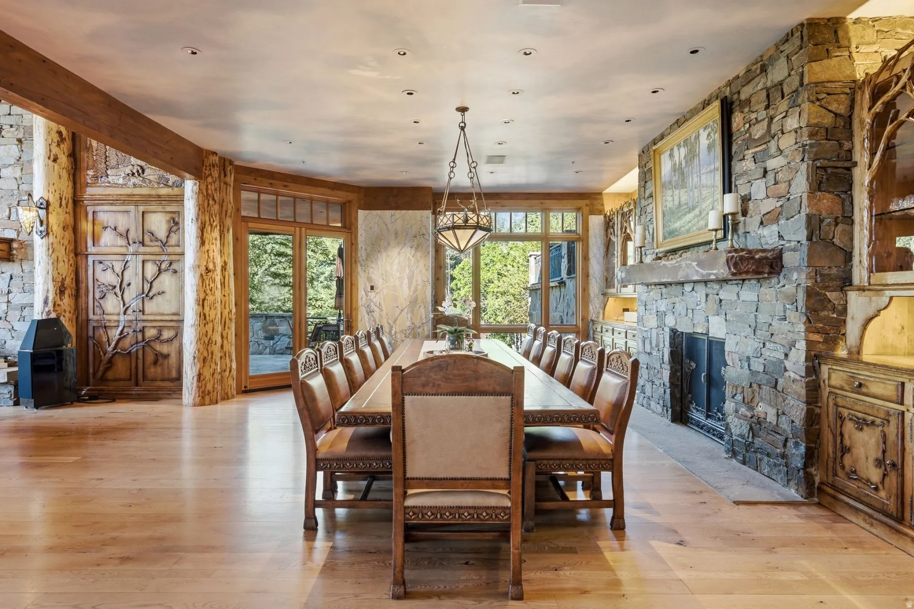 Spacious dining area featuring stone accent walls, natural wood-finish flooring, and a stone fireplace with a substantial mantel