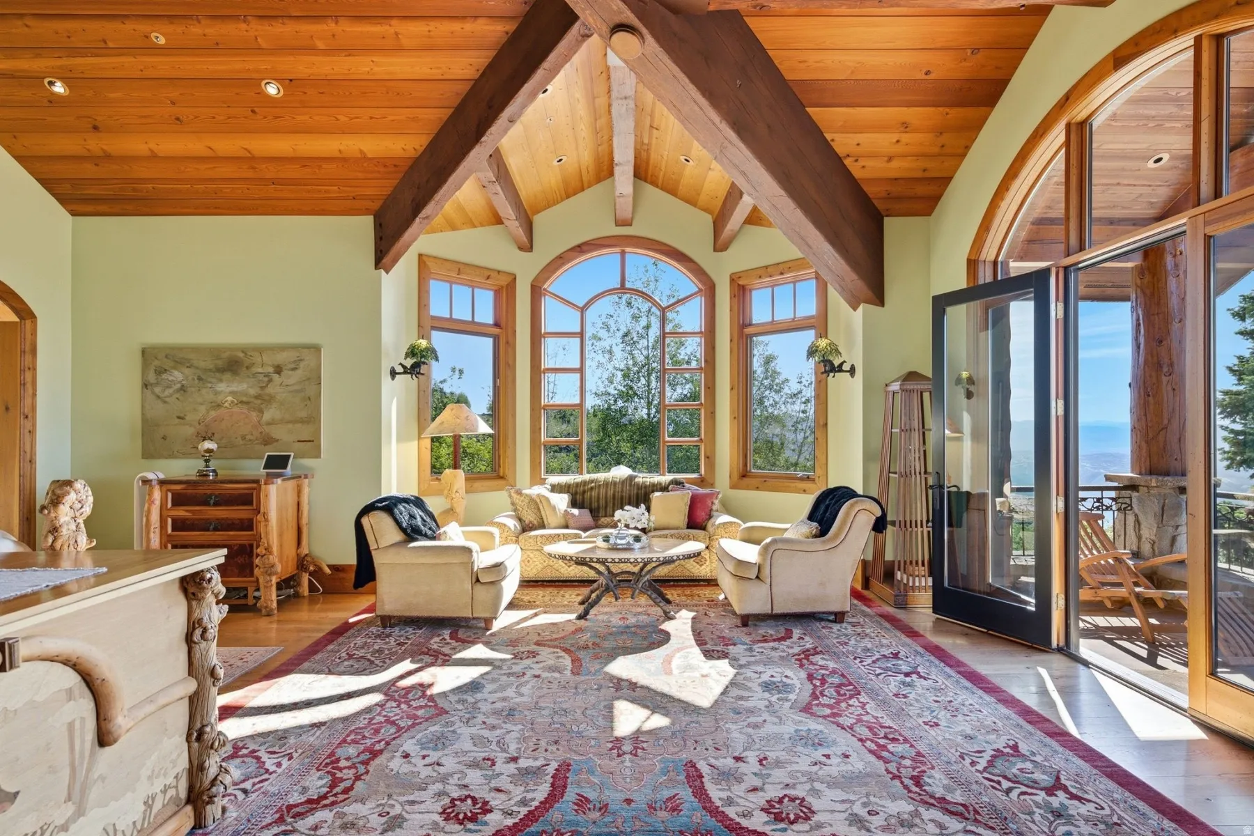Bright room featuring a vaulted wood-paneled ceiling with exposed wood beams, arched windows, light-colored walls, wood-finish flooring, and a glass-paneled double door opening to an exterior space