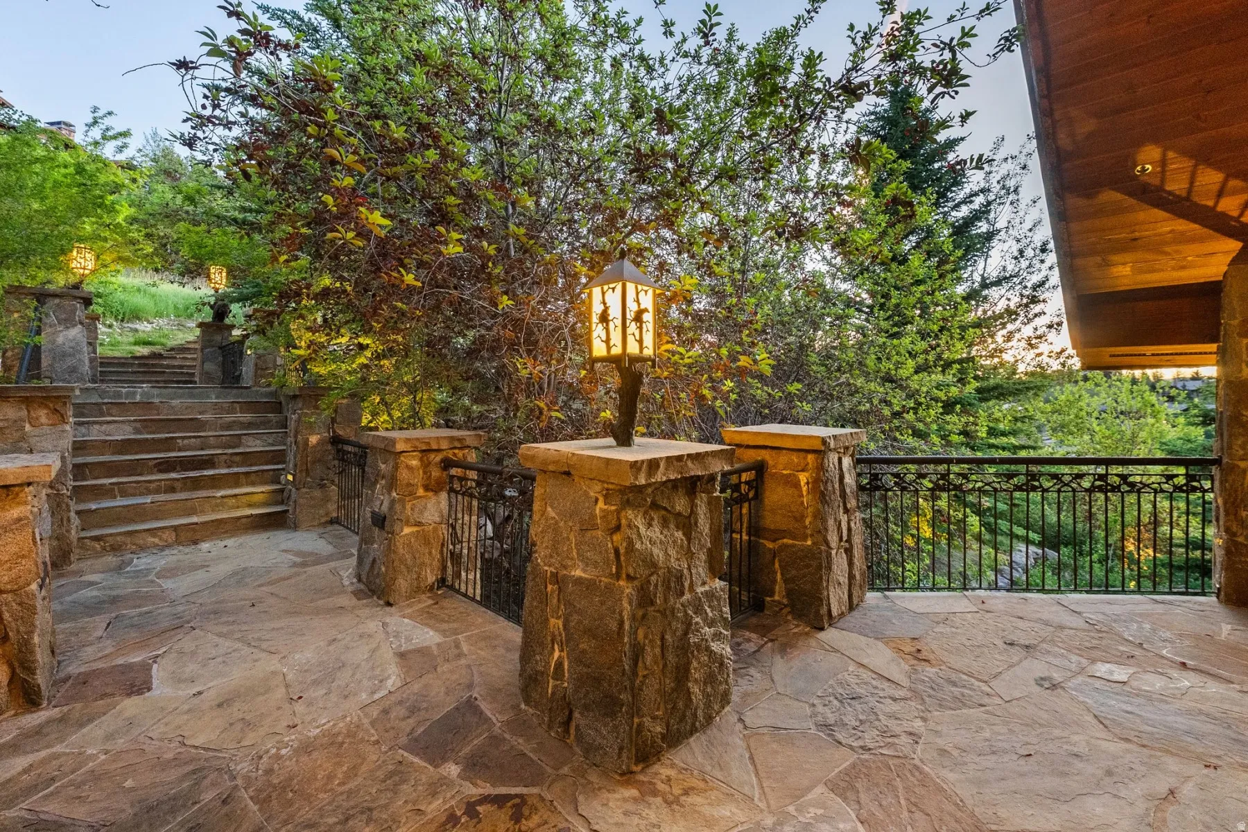 Stone patio with flagstone flooring, solid stone pillars, decorative exterior lighting, and an ornate metal railing