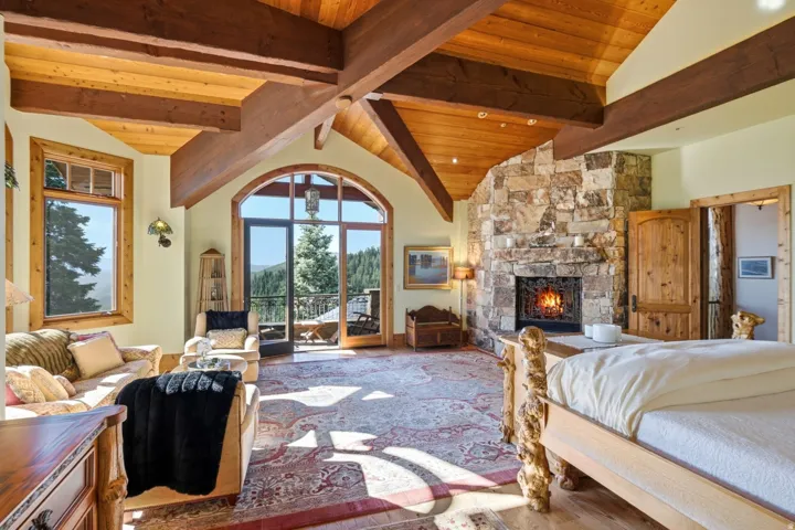 Spacious room featuring a stone-clad fireplace, exposed wood beams, vaulted wood-finish ceilings, an arched glass door, and large windows