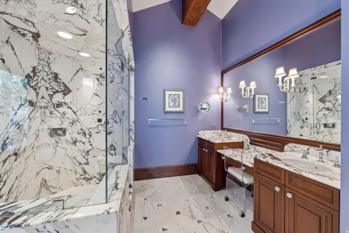 Spacious bathroom featuring a full-height marble shower enclosure with glass surround, double vanity with marble countertops, and an integrated dressing table