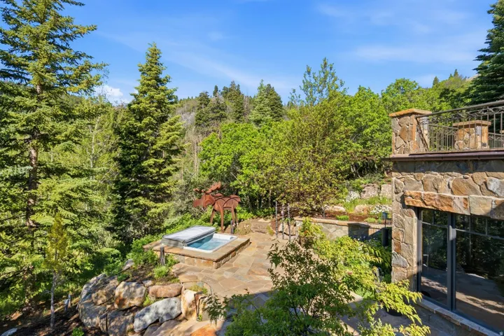Outdoor patio featuring an integrated hot tub with stone surround, complemented by a natural stone retaining wall and extensive mature trees
