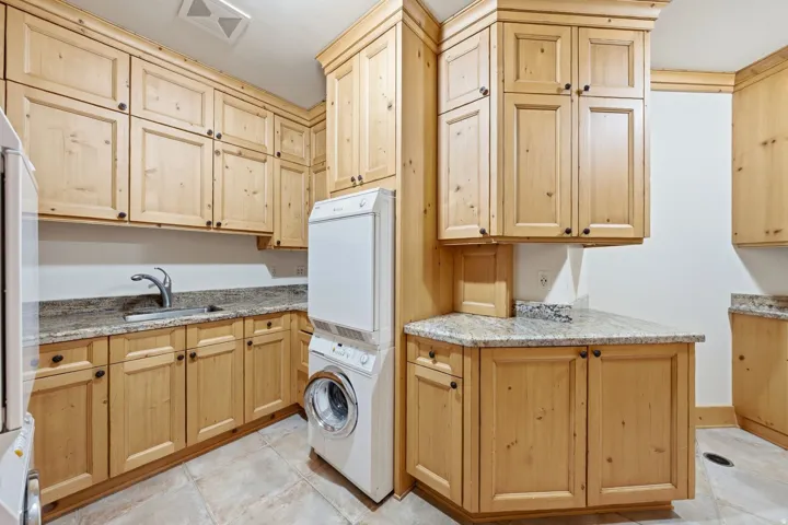 Utility room featuring extensive light wood cabinetry with dark hardware, granite countertops, a stainless steel sink with a gooseneck faucet, and tile flooring