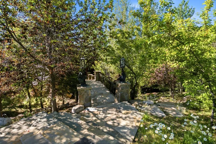 Terraced stone staircase featuring integrated stone posts with lanterns, surrounded by mature trees and natural landscaping