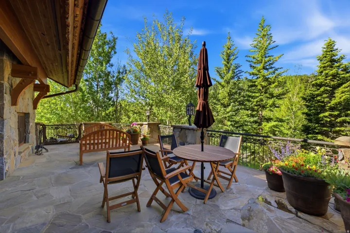 Expansive stone patio featuring a stone exterior wall, a wrought iron railing, and a tongue-and-groove wood ceiling with exposed beams