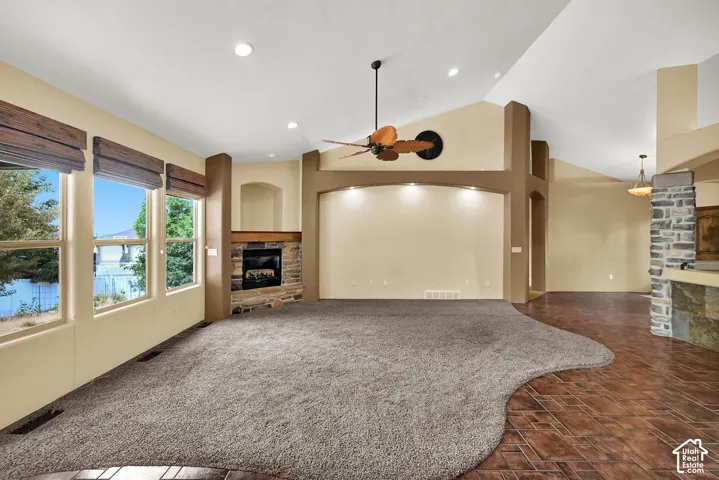 Spacious living area featuring a stone-clad fireplace with a wood mantel, vaulted ceilings, and recessed lighting