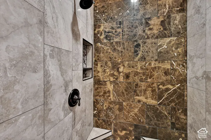 Enclosed shower featuring a dark marble-patterned tiled wall, light stone-look tiled wall, a built-in shower niche, and matte black fixtures