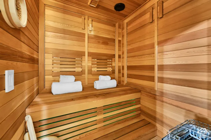 Wood-paneled sauna featuring built-in tiered seating, a wall-mounted temperature control unit, and slatted backrests