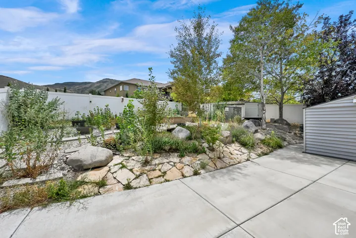 Expansive concrete patio area with a stone-accented garden bed featuring natural rock elements and mature trees