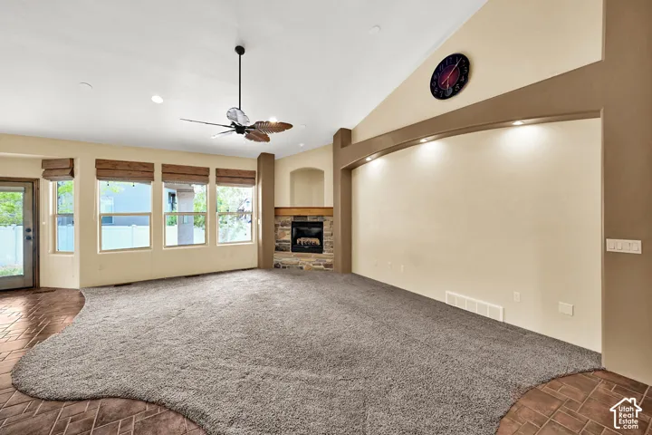 Vaulted ceiling living space featuring a stone-surround fireplace with a wood mantle, a ceiling fan, recessed lighting, and multiple windows with wood blinds