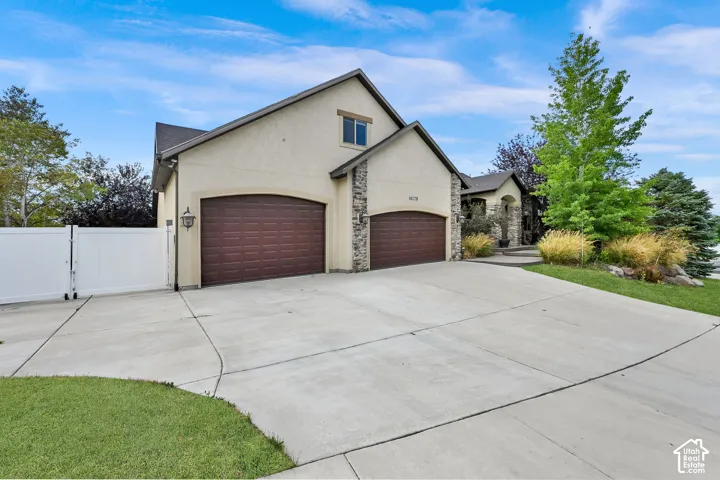 Stucco and stone exterior with a concrete driveway leading to two arched garage doors