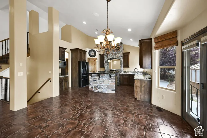 Expansive great room featuring patterned tile flooring, a stone-clad kitchen island, dark wood cabinetry, a wrought iron chandelier, and a balcony access door